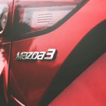 Closeup of the back of a red Mazda car with the Mazda 3 logo on it .